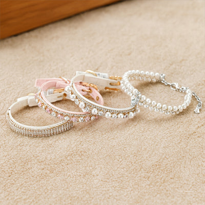 quatre colliers chien perles strass cristal blanc et rose posés sur tapis beige